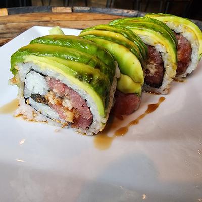 Sushi roll wrapped in sliced avocado with tuna inside, drizzled with sauce