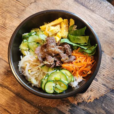 Bibimbap bowl with beef, cucumber, carrots, bean sprouts, egg and greens over rice