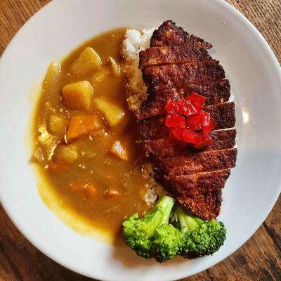 Plate of Japanese curry with a sliced tonkatsu pork cutlet, potatoes and broccoli