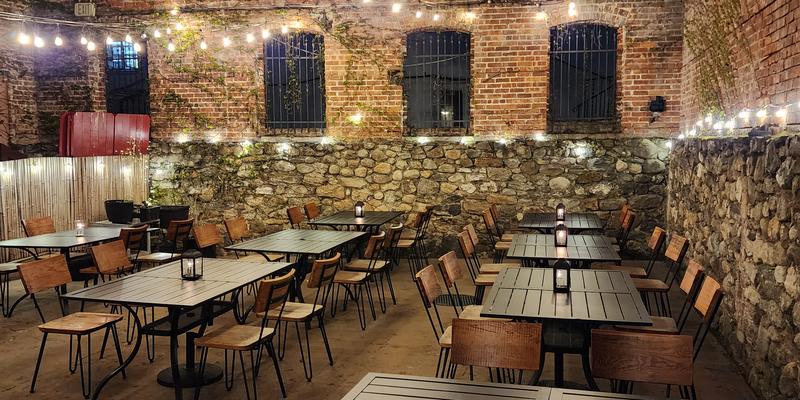 Patio seating under string lights between brick walls at night