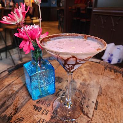 Pink martini with chocolate drizzle beside a blue vase of pink flowers