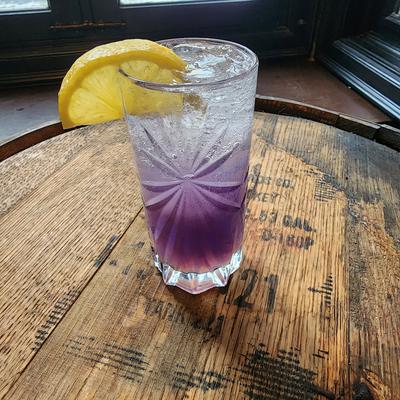 Tall purple drink over ice with a lemon wheel on a wooden table