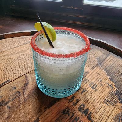 Cocktail with a red sugar rim and a lime wedge in a blue-tinted glass