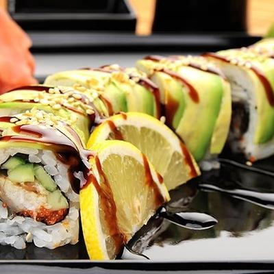 Sushi roll topped with sliced avocado on a black plate with pickled ginger