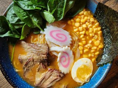 Tom Yum ramen with sliced pork, corn, spinach, narutomaki and a halved egg in a spicy orange broth