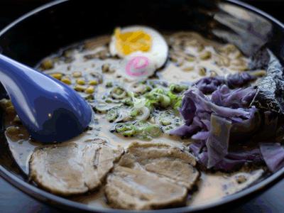 Tonkotsu ramen in a dark bowl with sliced pork, soft egg, scallions and a blue spoon